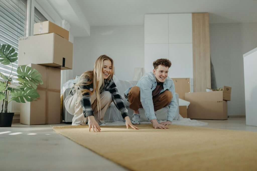 Cheerful young couple in their new apartment, rolling out carpet. Conception of moving.